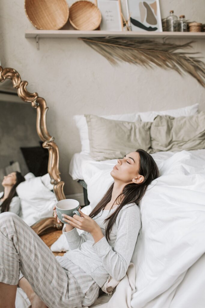 Woman relaxing softly in bed in the morning, holding a warm cup of tea
