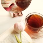A gold-rimmed mirror reflecting a cup of tea and a pink tulip, an aesthetic still life