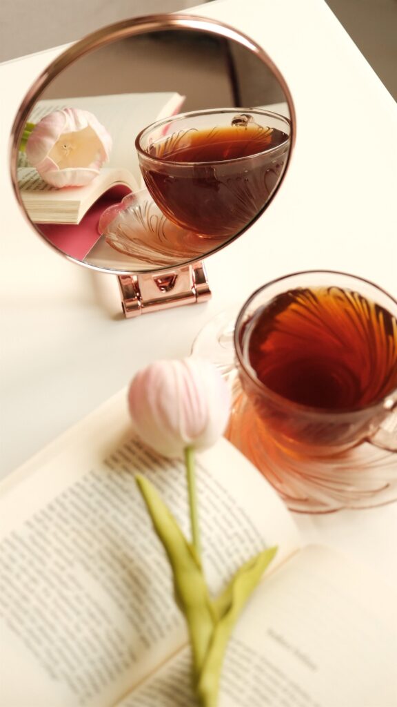 A gold-rimmed mirror reflecting a cup of tea and a pink tulip, an aesthetic still life