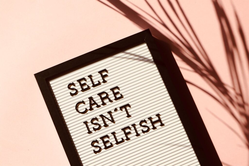 A letterboard sign reading 'self care isn't selfish' against a soft pink wall