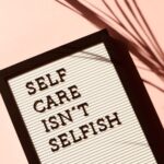 A letterboard sign reading 'self care isn't selfish' against a soft pink wall